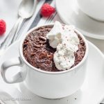 Keto chocolate cake in a cup with melted chocolate, whipped cream, and raspberries.